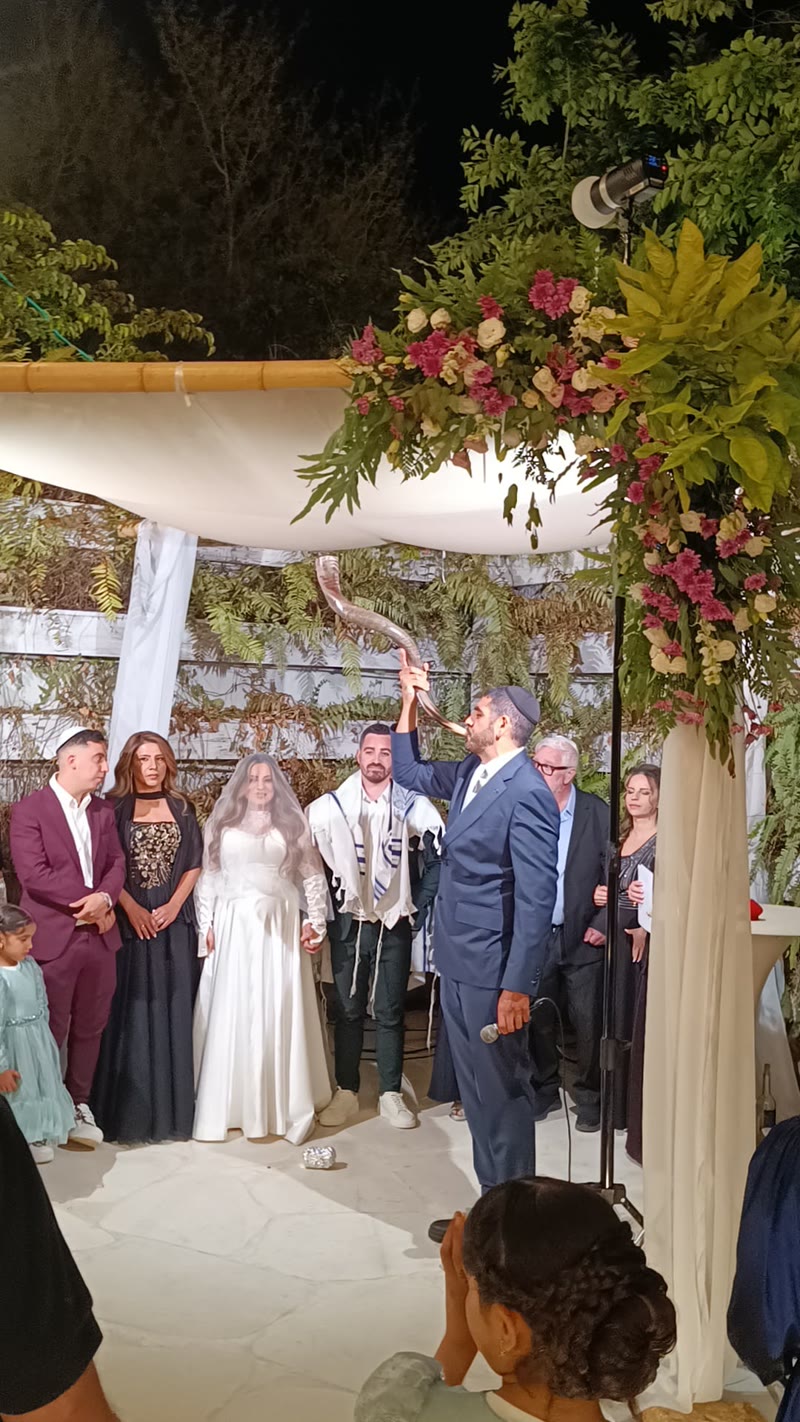 הרב חיים חורי עורך חופה תחת חופת פרחים מוארת, החתן והכלה והאורחים סביב